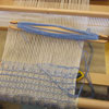 Rigid heddle loom with shuttle and blue and white woven fabric